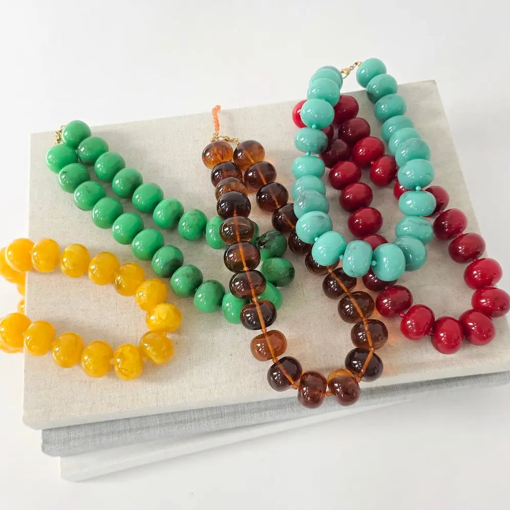 Colorful chunky beaded necklaces in yellow, green, amber, and turquoise on a white display.