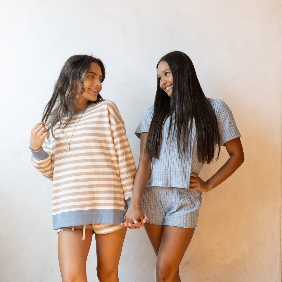 Two young women smiling and holding hands, wearing comfortable loungewear sets.