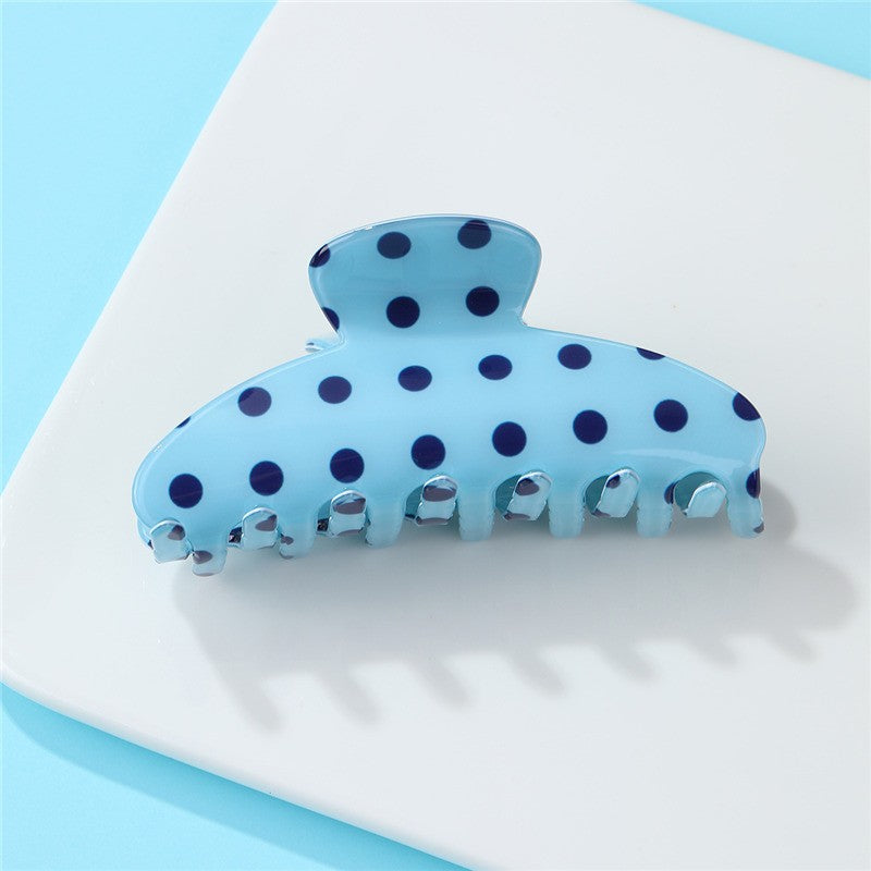 Blue hair clip with black polka dots on a white surface with a light blue background