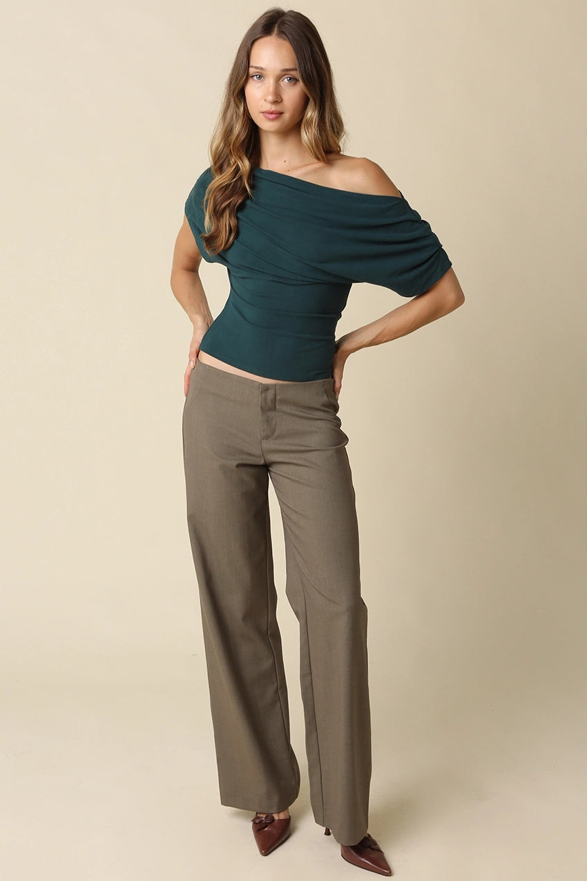 Woman wearing a green off-shoulder top and beige pants on a beige background