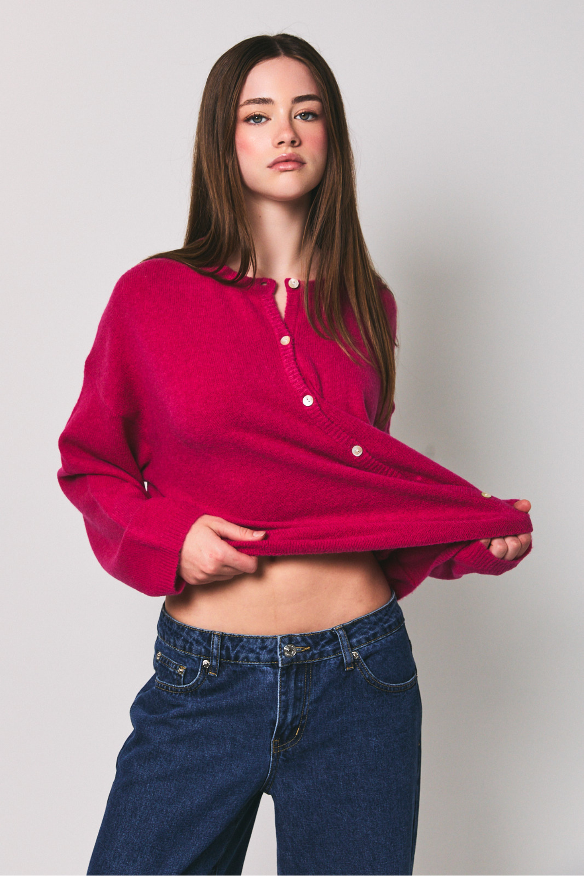 Woman wearing a bright pink shirt and blue jeans against a plain background