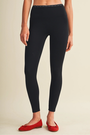 A model wearing black high-waisted leggings with a studded waistband, paired with red ballet flats, shown from the waist down against a light beige background.