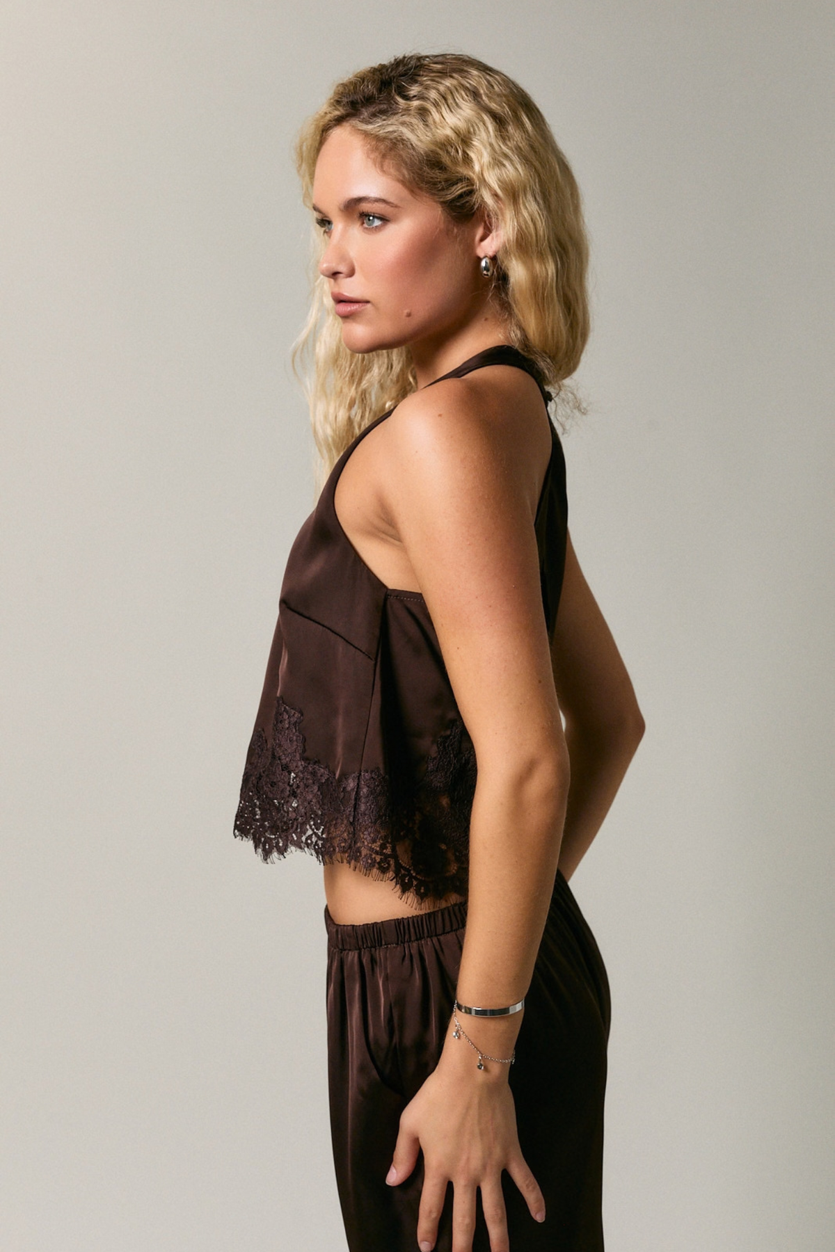 Woman wearing a brown lace top and pants against a plain background