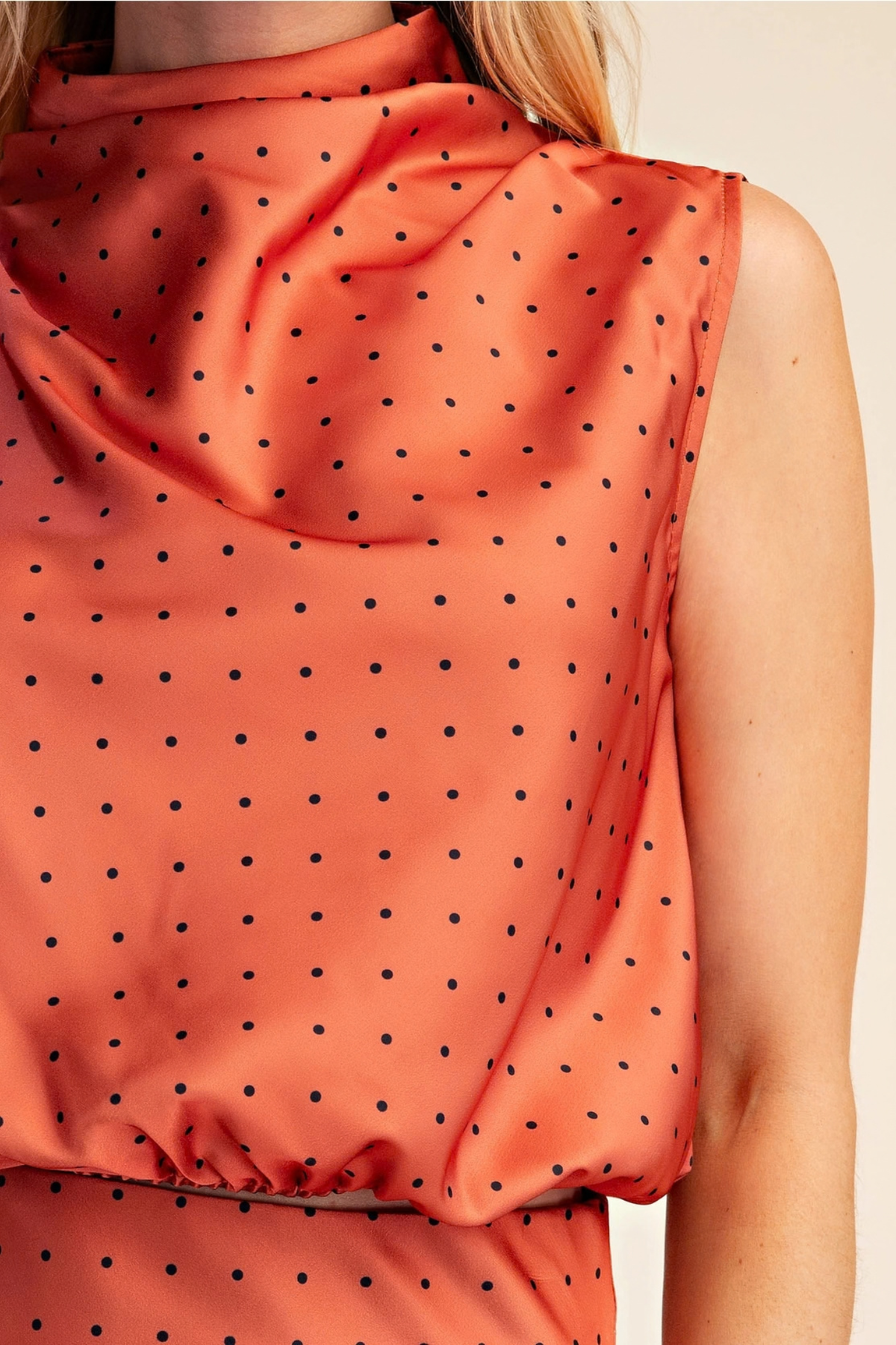 Close-up of a sleeveless high-neck top in a peachy orange color with a black polka dot pattern, worn by a model.