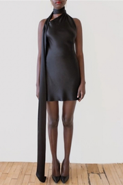 Person wearing a black sleeveless dress with a long black scarf against a white background