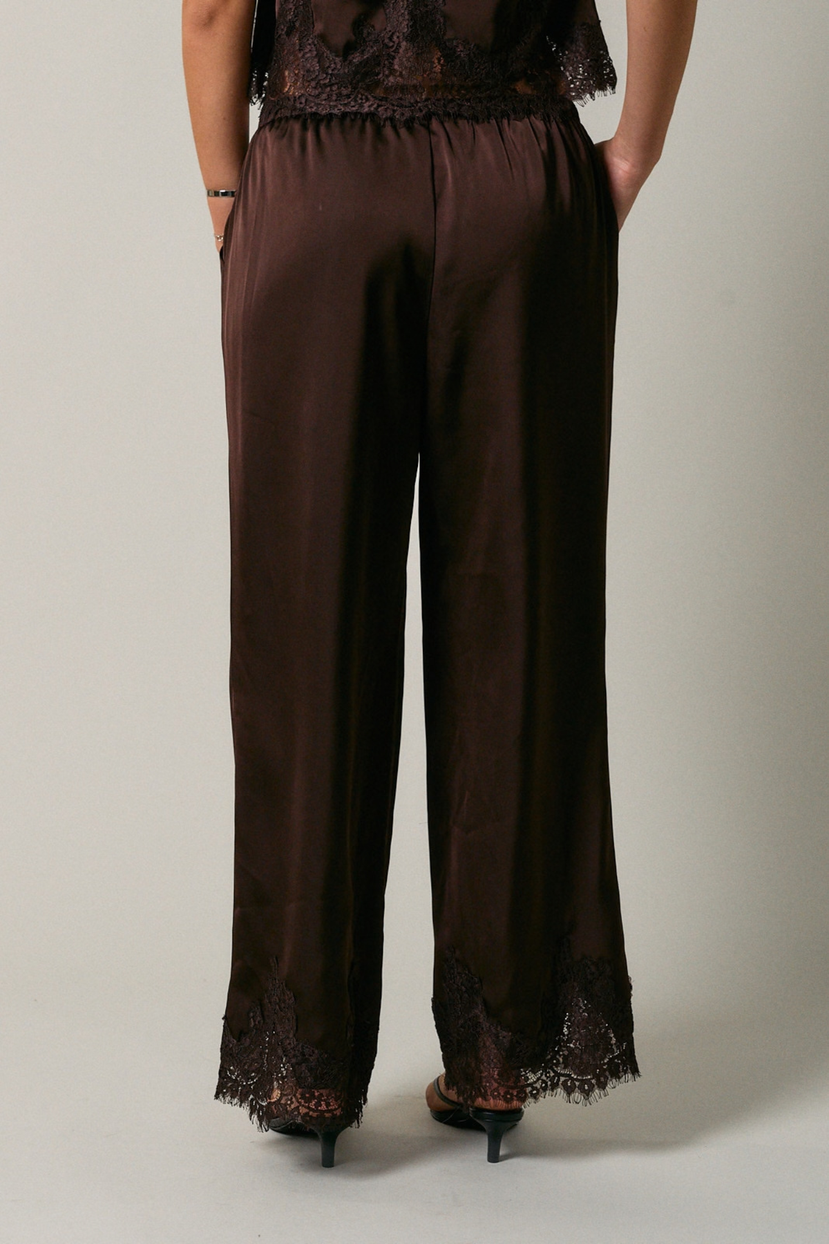 Brown pants with lace trim worn by a person on a plain background