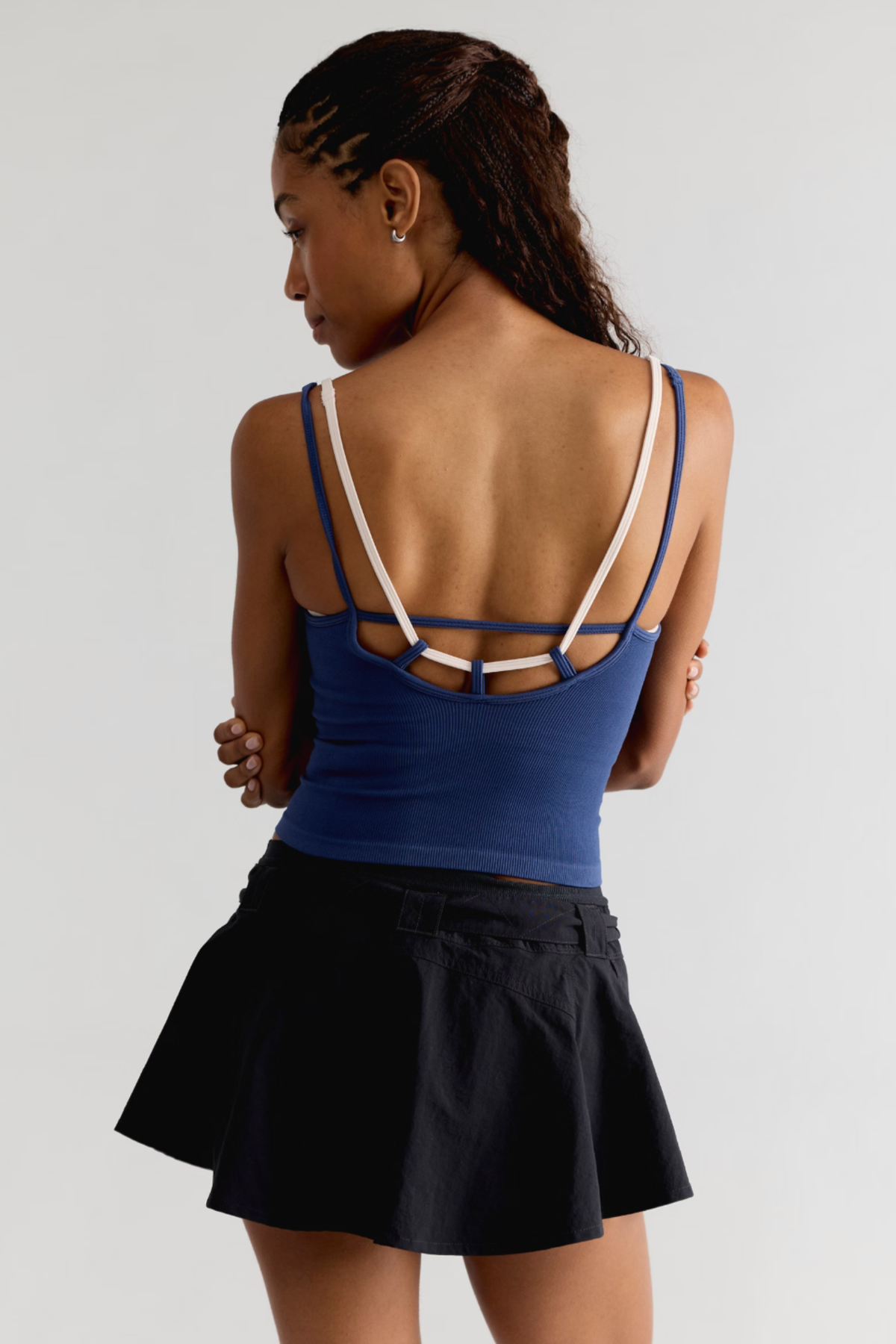 A woman shown from the back wearing a royal blue athletic tank top with white contrast straps and a black tennis skirt, against a light gray studio background.