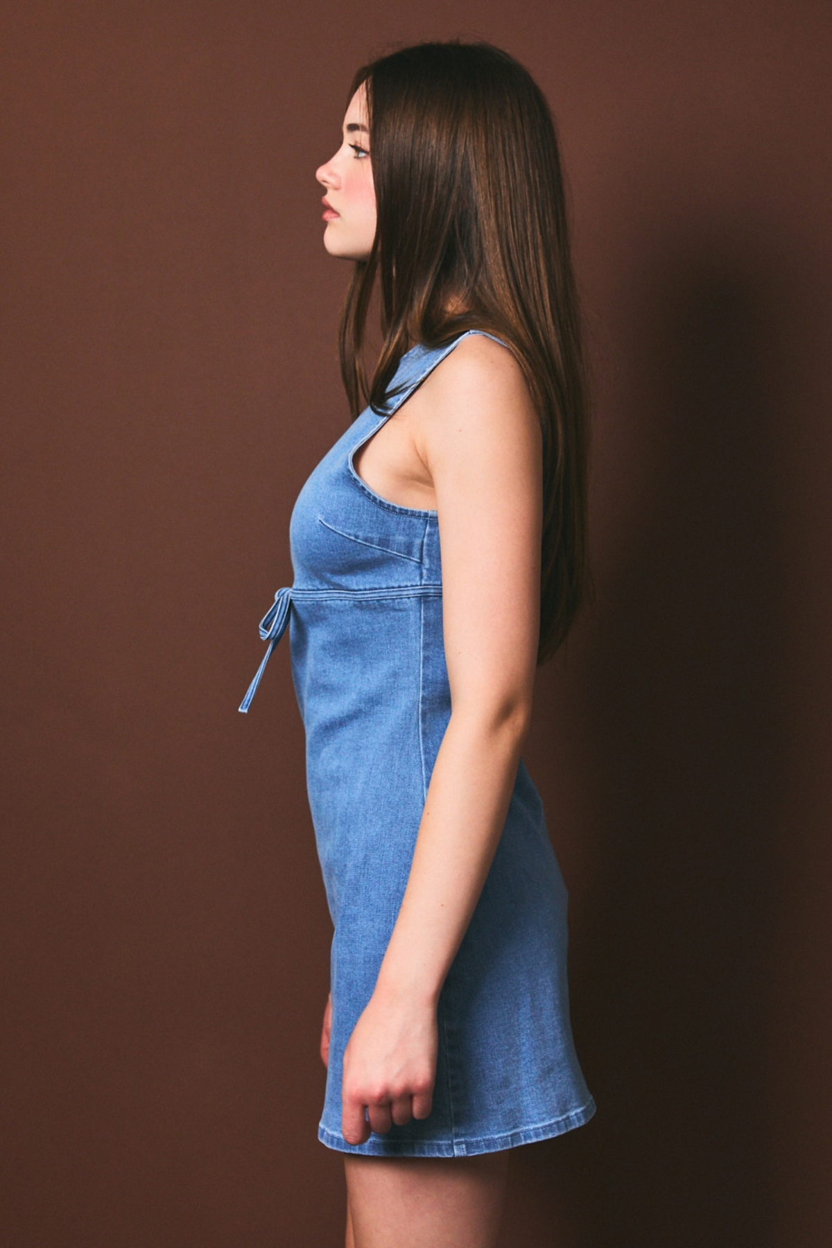 Woman wearing a blue denim dress against a brown background