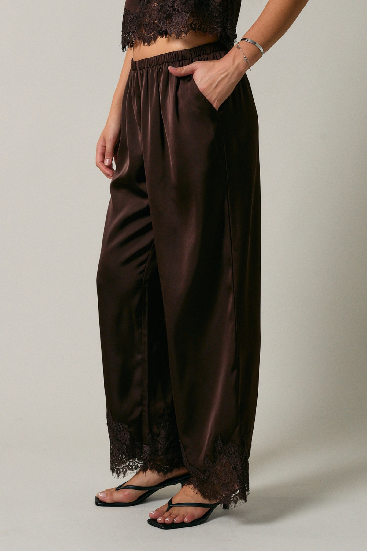 Brown satin pants with lace trim worn by a person on a plain background
