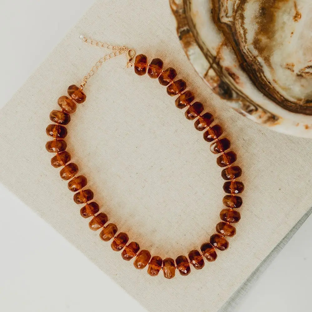 Brown beaded necklace on a textured surface with an oyster shell in the background