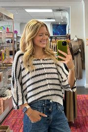 A woman takes a mirror selfie in a clothing boutique, wearing a black and white striped knit cardigan sweater and blue jeans.