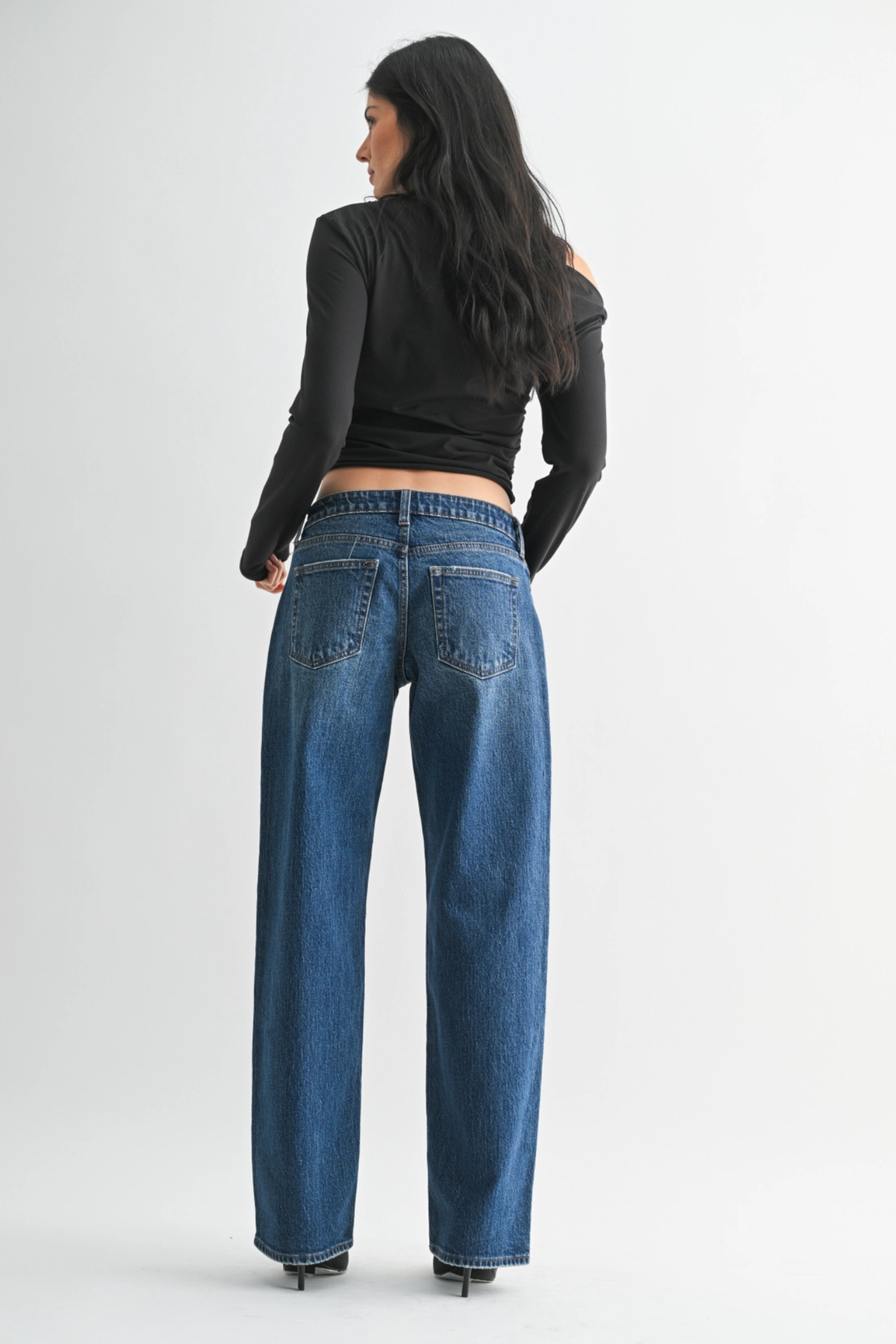 Person wearing blue jeans and a black long-sleeve top on a white background