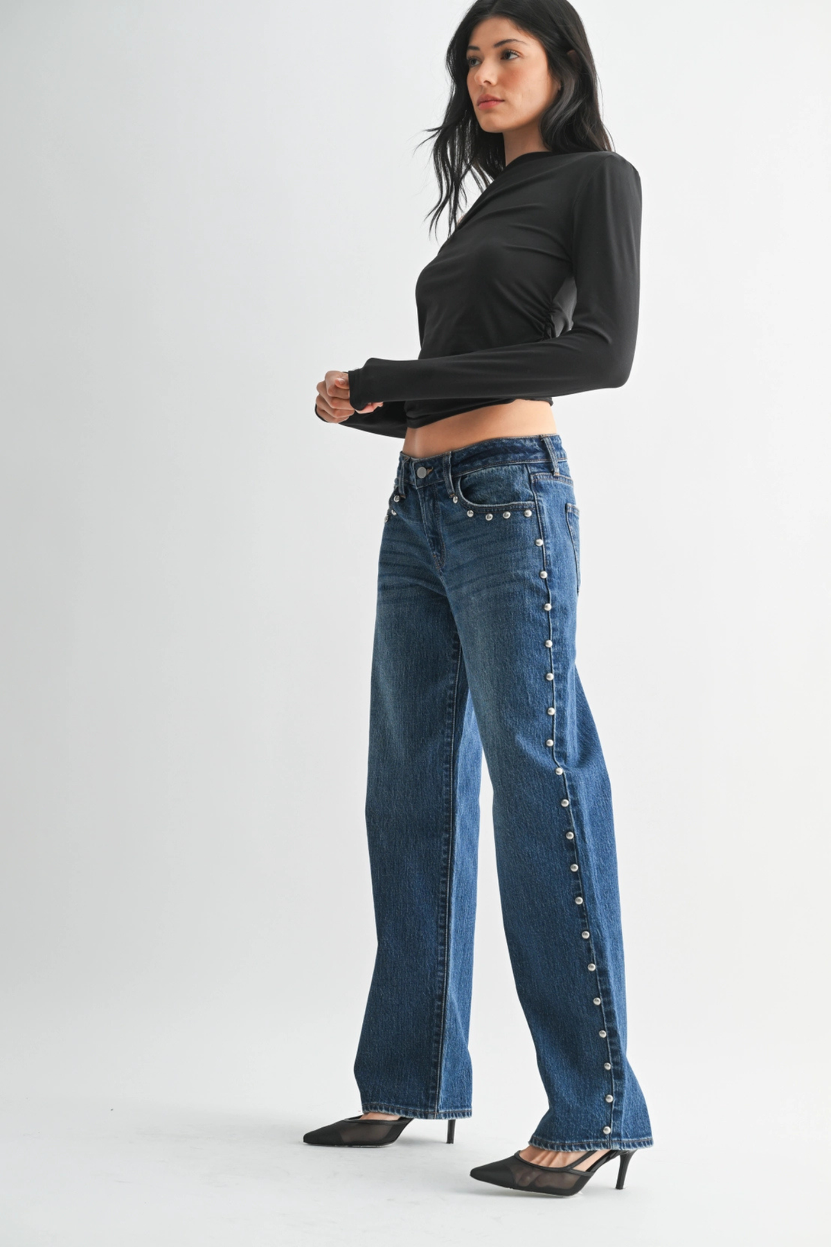 Woman wearing studded blue jeans and a black long-sleeve top on a white background