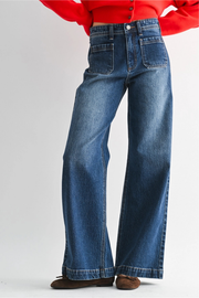 A person wearing high-waisted, wide-leg blue denim jeans with a red cropped top and brown shoes, shown from the waist down against a light gray studio background.