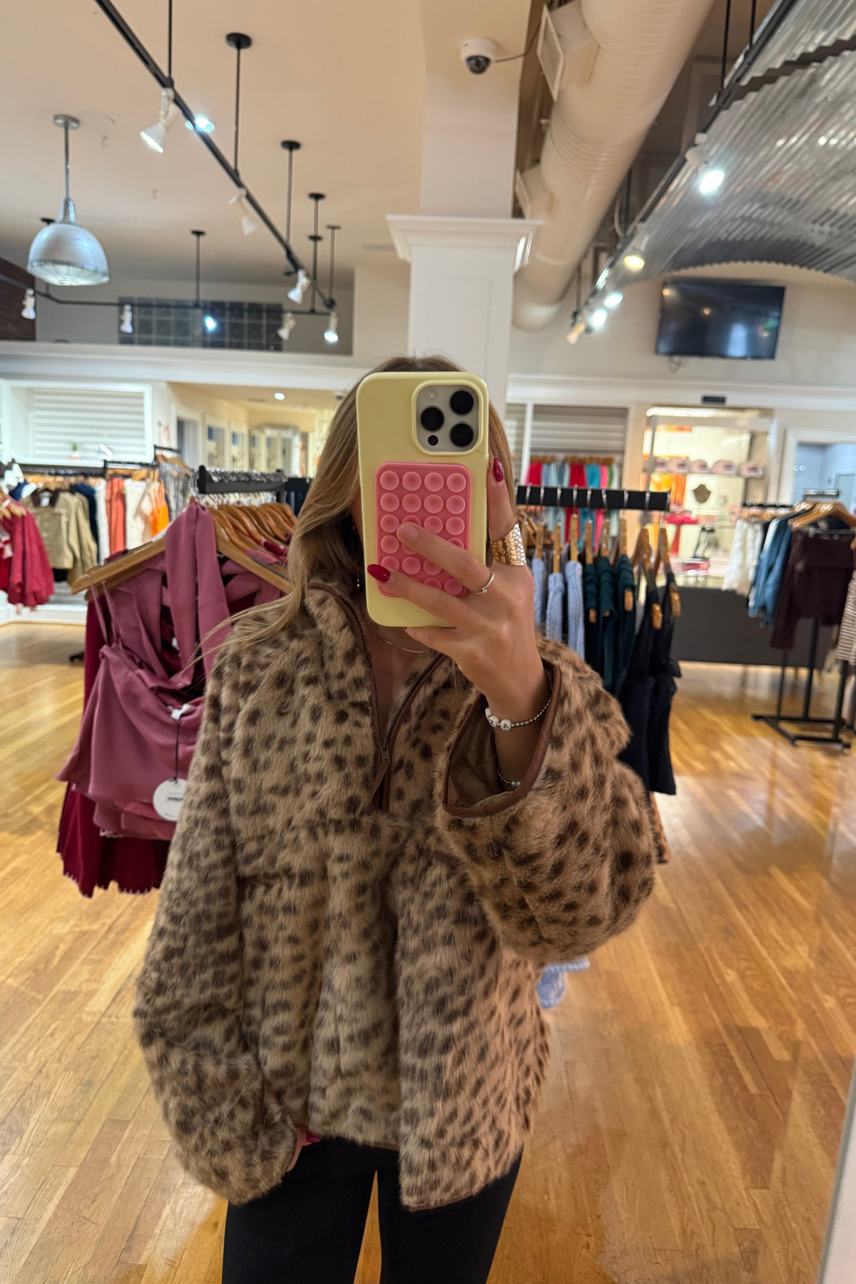 A woman takes a mirror selfie at J.Cole Shoes in Stillwater wearing a fuzzy leopard-print jacket. The jacket has a warm tan base with black leopard spots.
