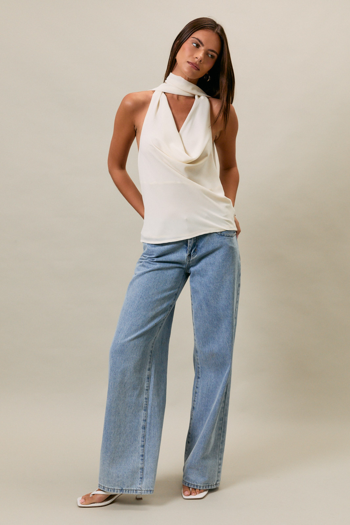 Woman wearing a white sleeveless top and blue jeans against a plain background