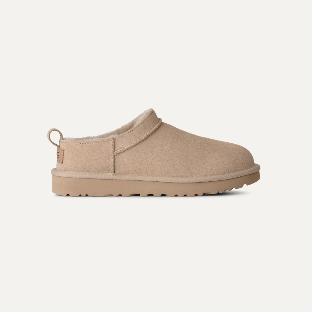 A single UGG slip-on clog shoe in a light tan suede-like material with a matching sole and a small heel pull tab, shown in profile against a plain off-white background.