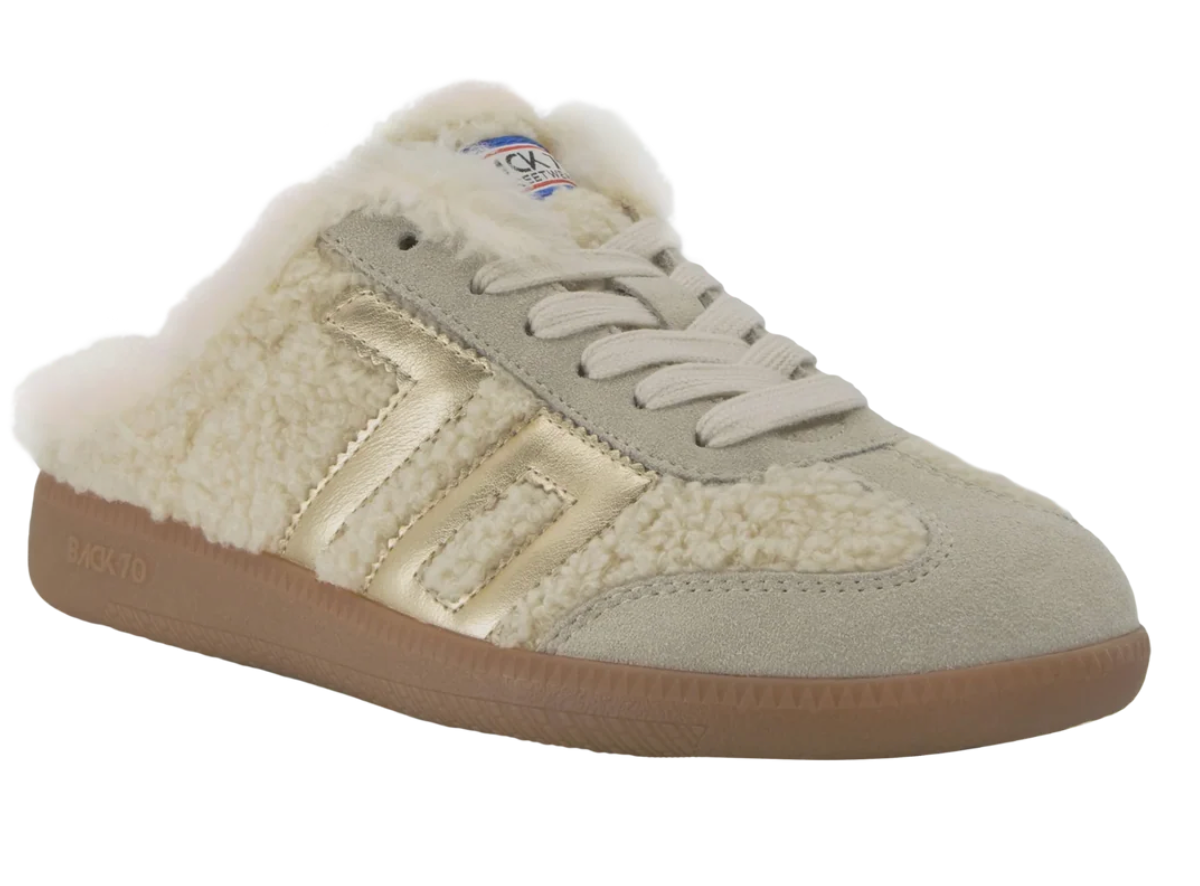 A low-top slip-on sneaker with a cream sherpa fleece lining, light beige suede upper, metallic gold side stripes, beige laces, and a brown gum sole. The brand name 'BACK TO' is visible on the side of the sole.