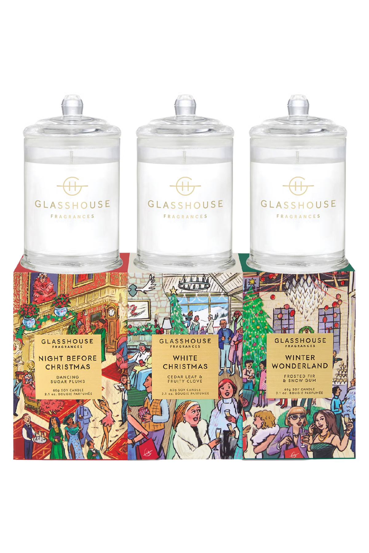 Three GLASSHOUSE Fragrances candles in clear glass jars with white wax and gold lettering, displayed on top of a colorful illustrated gift box. The box features holiday-themed illustrations and labels for 'Night Before Christmas', 'White Christmas', and 'Winter Wonderland'.