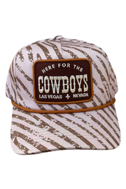 A baseball cap featuring a brown and off-white distressed zebra-like pattern, with a prominent brown patch on the front that reads 'HERE FOR THE COWBOYS LAS VEGAS + NEVADA'.
