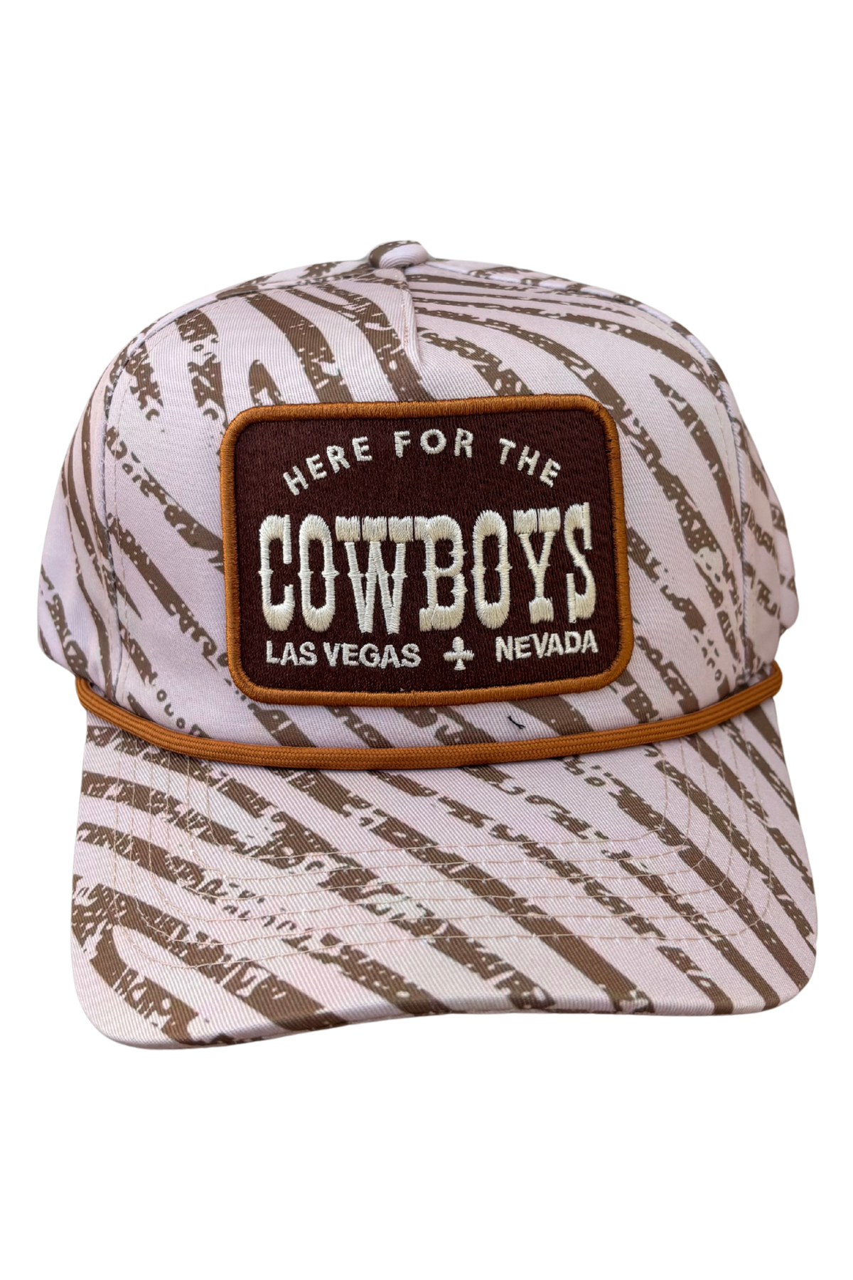 A baseball cap featuring a brown and off-white distressed zebra-like pattern, with a prominent brown patch on the front that reads 'HERE FOR THE COWBOYS LAS VEGAS + NEVADA'.