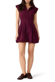 A woman modeling a sleeveless, button-front mini dress in deep burgundy with a flared skirt, paired with dark brown loafers, against a plain white background.