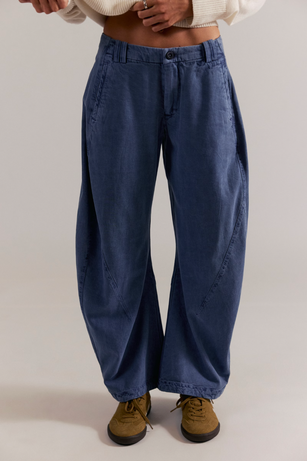Person wearing blue wide-leg jeans and brown shoes on a plain background