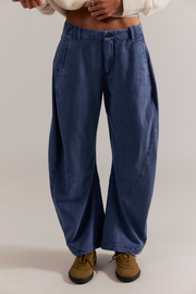 Person wearing blue wide-leg jeans and brown shoes on a plain background