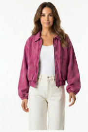 A woman modeling a washed magenta-purple cropped jacket over a white tank top and cream-colored pants, set against a plain white studio background.