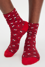Red crew socks with a black geometric diamond pattern and small white cherry motifs, shown on a model's feet against a plain white background.
