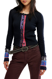 A woman wearing a black long-sleeve knit cardigan with a colorful vertical button placket and patterned cuffs, paired with brown pants and a studded belt, against a plain white background.