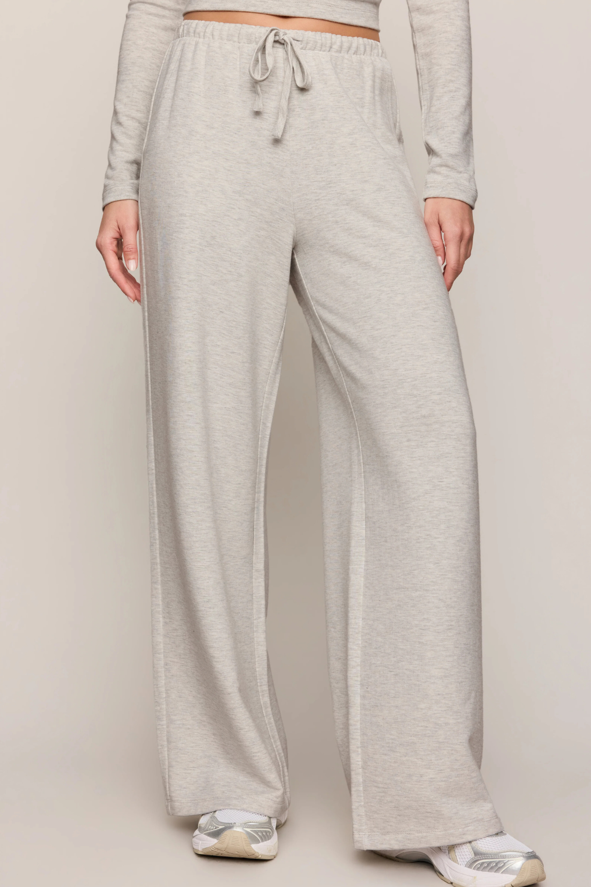 A person wearing light heather gray wide-leg sweatpants with a drawstring waist, shown from the waist down against a plain light beige studio background.