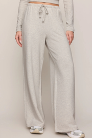 A person wearing light heather gray wide-leg sweatpants with a drawstring waist, shown from the waist down against a plain light beige studio background.