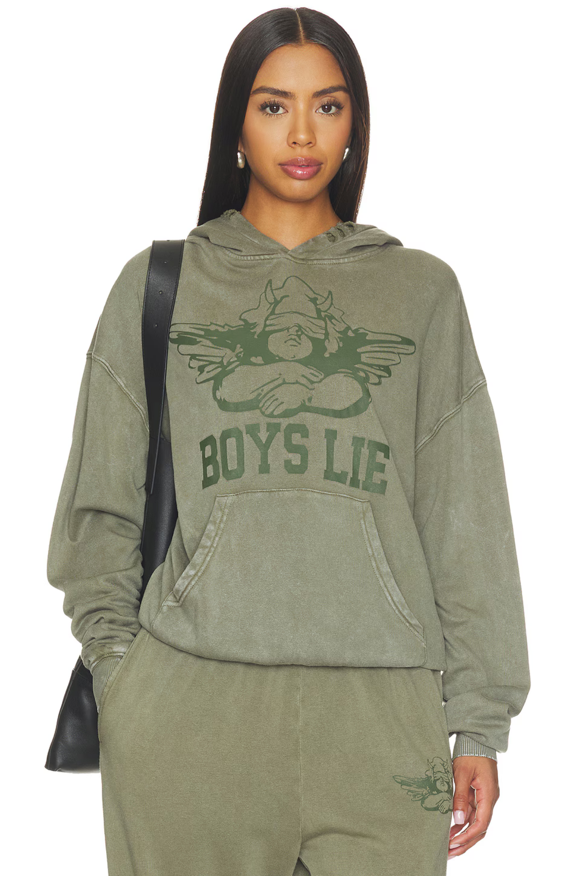 A woman modeling an olive green hooded sweatshirt and matching sweatpants set. The hoodie features a dark green graphic of a winged figure with the text 'BOYS LIE' across the chest.
