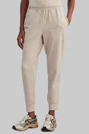 Beige jogger sweatpants with an elastic waistband and cuffs, shown on a model wearing athletic sneakers against a solid gray background.
