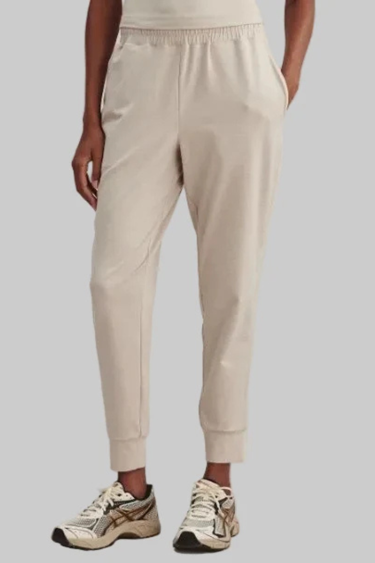 Beige jogger sweatpants with an elastic waistband and cuffs, shown on a model wearing athletic sneakers against a solid gray background.