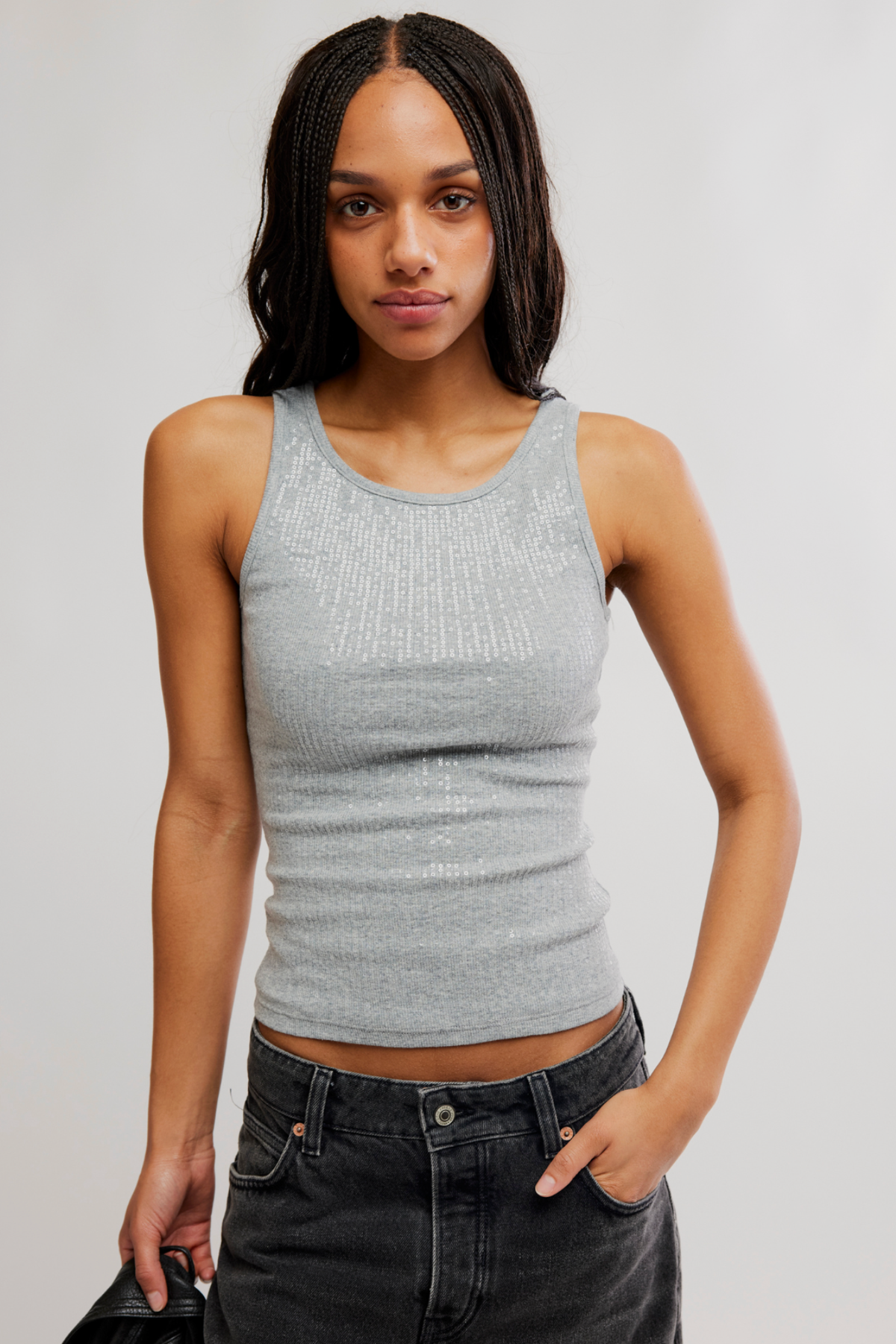 A woman modeling a light gray ribbed knit tank top paired with dark gray jeans against a plain light gray studio background.
