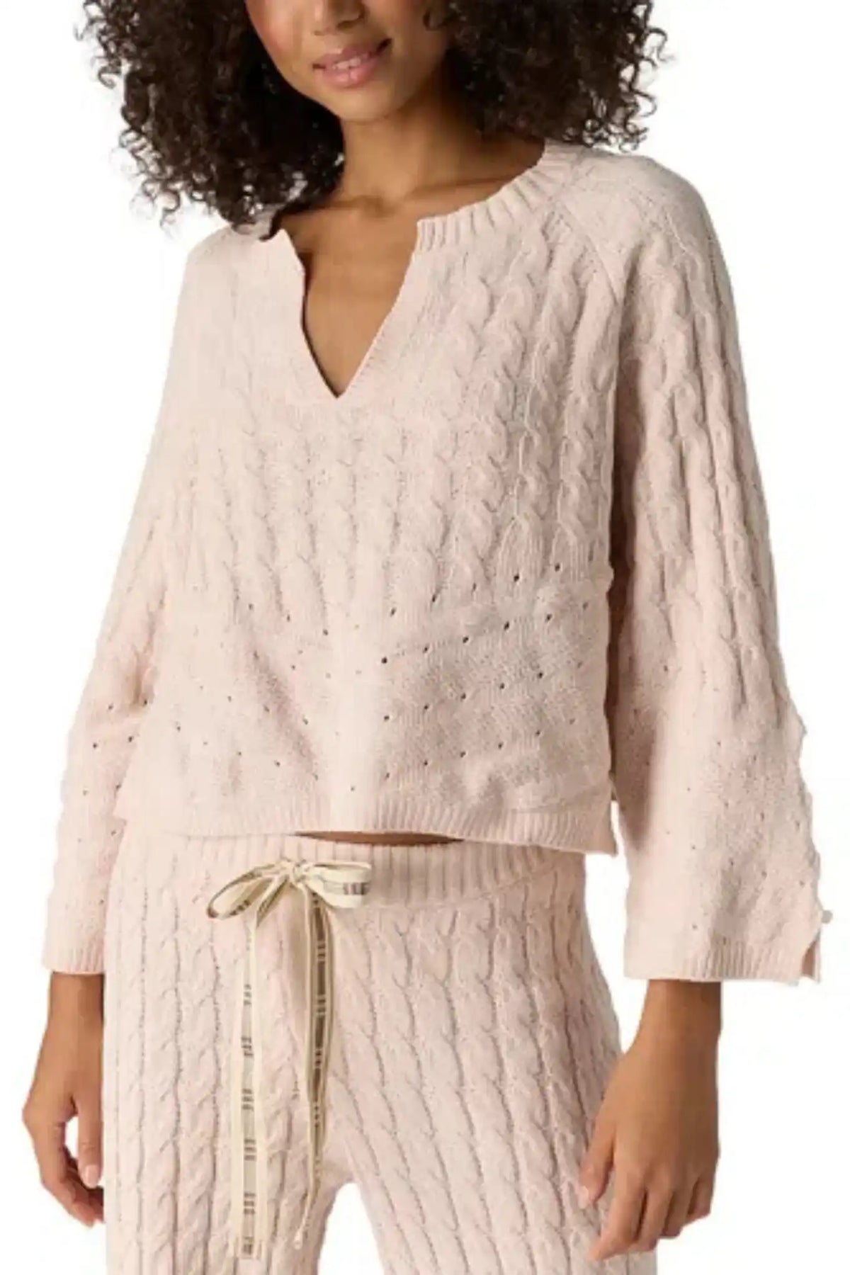 A woman wearing a light blush pink cable-knit sweater and matching knit pants with a drawstring waist, shown against a plain white background.