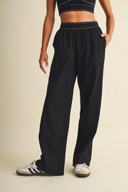 A person wearing loose black wide-leg sweatpants with a matching black crop top and white sneakers, standing against a plain beige studio background.