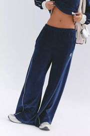 A person wearing navy blue wide-leg velour sweatpants with white piping along the sides, paired with a matching navy top and white sneakers, shown against a plain white studio background.