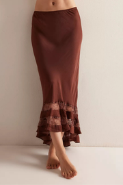 A woman wearing a rust-brown satin midi skirt with a ruffled tulle hem, shown from the waist down against a plain off-white wall.