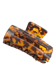 A tortoiseshell hair claw clip with a glossy amber, orange, and dark brown pattern, shown on a plain white background.