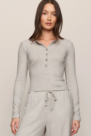 A woman modeling a light heather gray long-sleeve henley top with matching drawstring sweatpants against a plain beige studio background.
