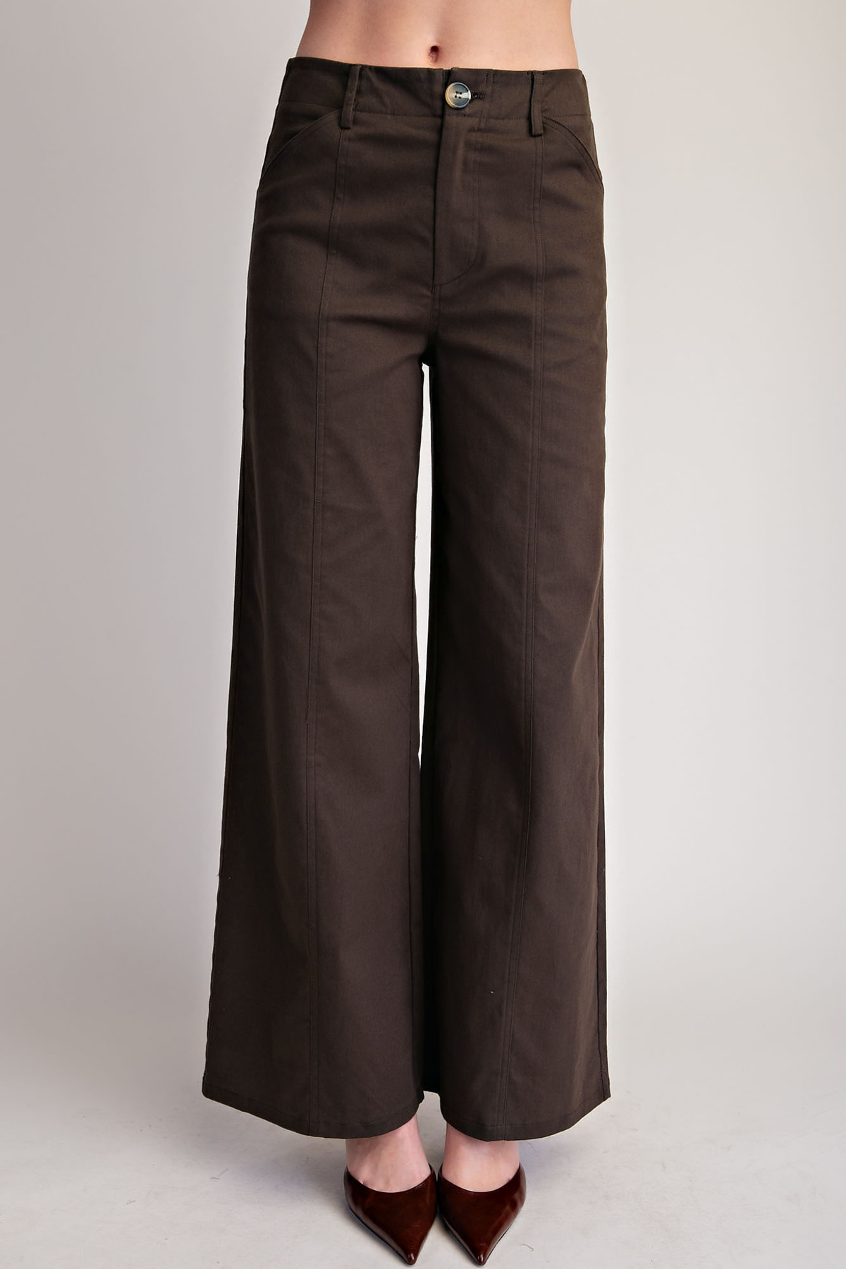 A person wearing dark brown wide-leg cropped pants with a button waistband, shown from the waist down against a light gray studio background.