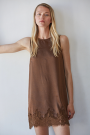 Woman wearing a brown sleeveless dress with lace trim against a white background