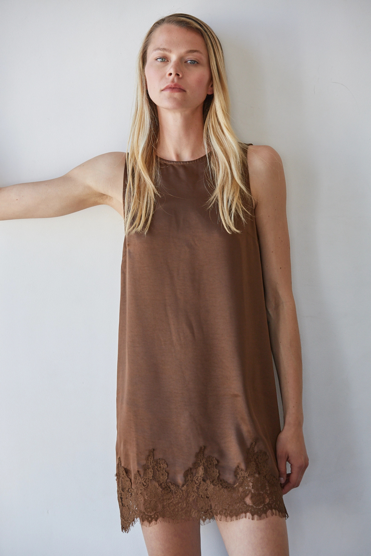 Woman wearing a brown sleeveless dress with lace trim against a white background