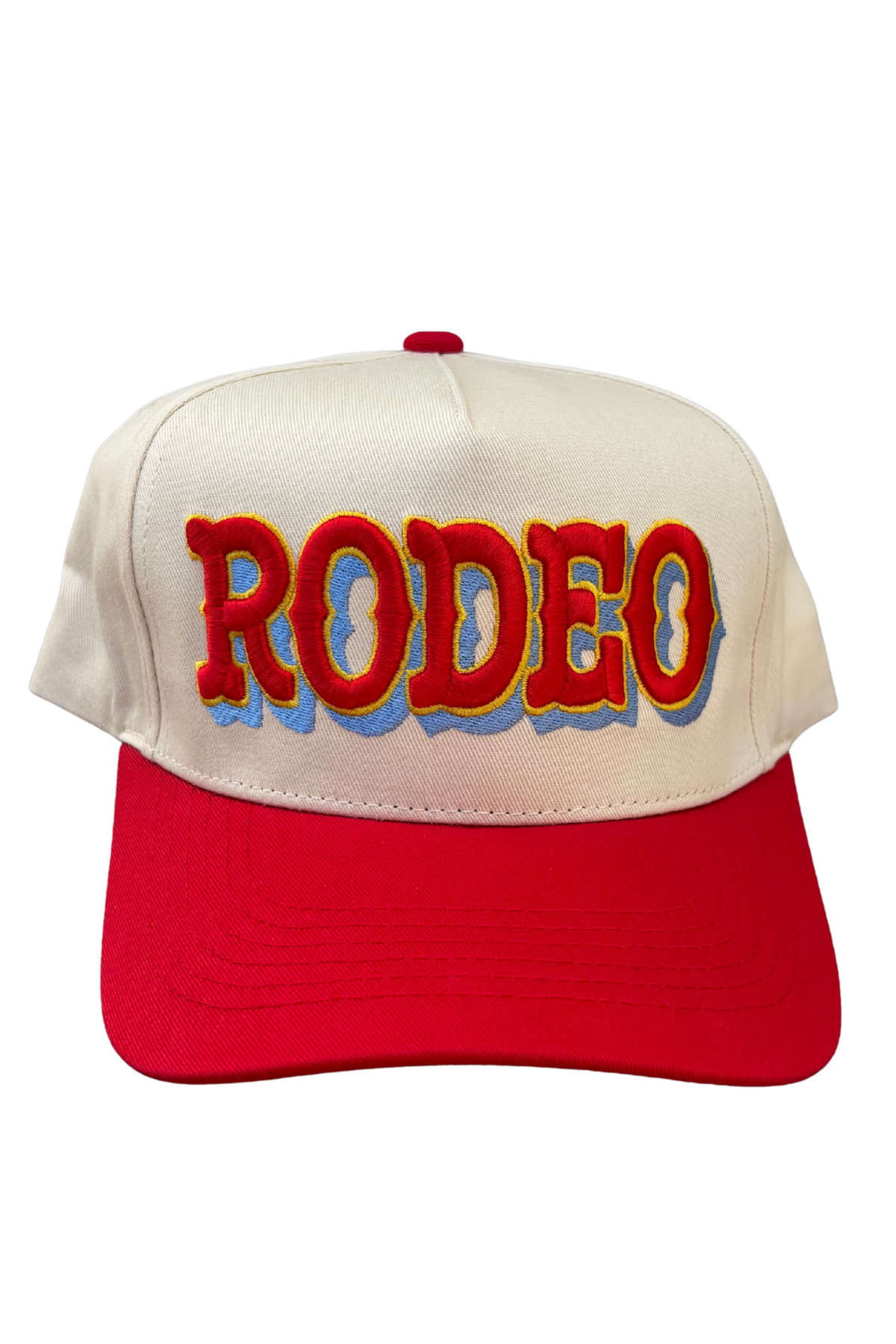 A two-tone baseball cap with an off-white crown and a bright red visor. The front of the crown features the word 'RODEO' embroidered in large red letters with a yellow outline and a blue shadow effect.