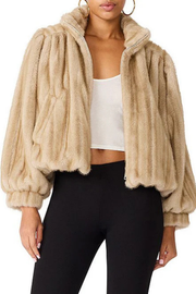 A woman wearing a beige faux fur cropped jacket with voluminous sleeves, styled over a white crop top and black leggings.