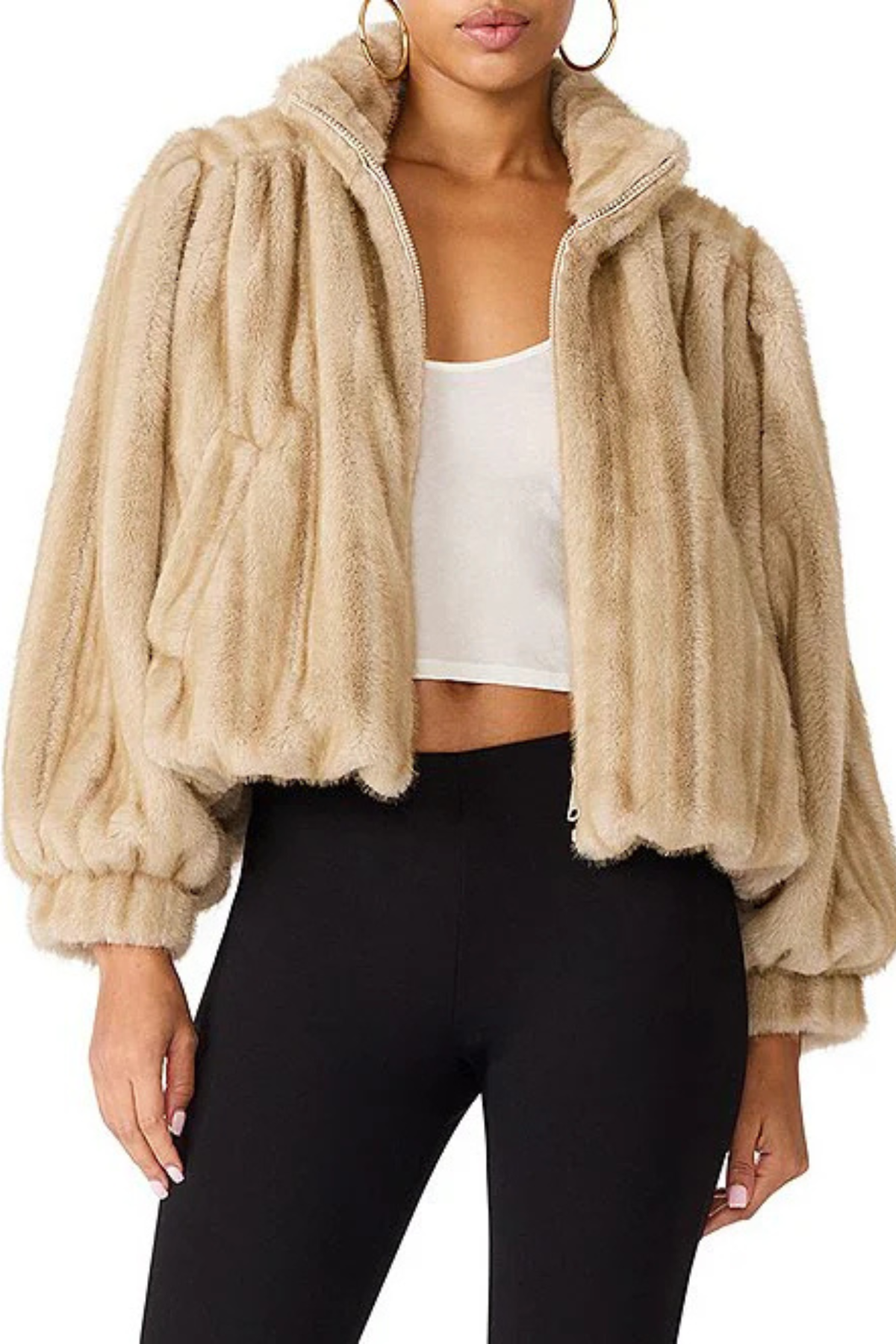 A woman wearing a beige faux fur cropped jacket with voluminous sleeves, styled over a white crop top and black leggings.