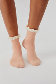 A pair of light peach ribbed ankle socks with white lace ruffle trim, shown on a model's feet against a light gray background.